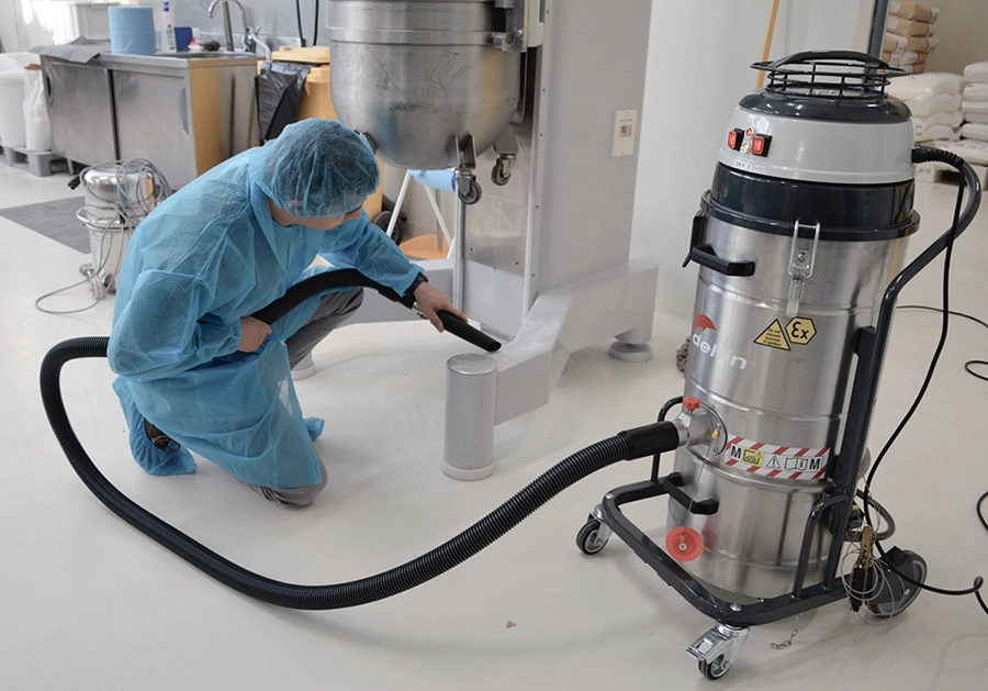Operator in blue PPE using a Delfin ATEX vacuum cleaner for cleaning