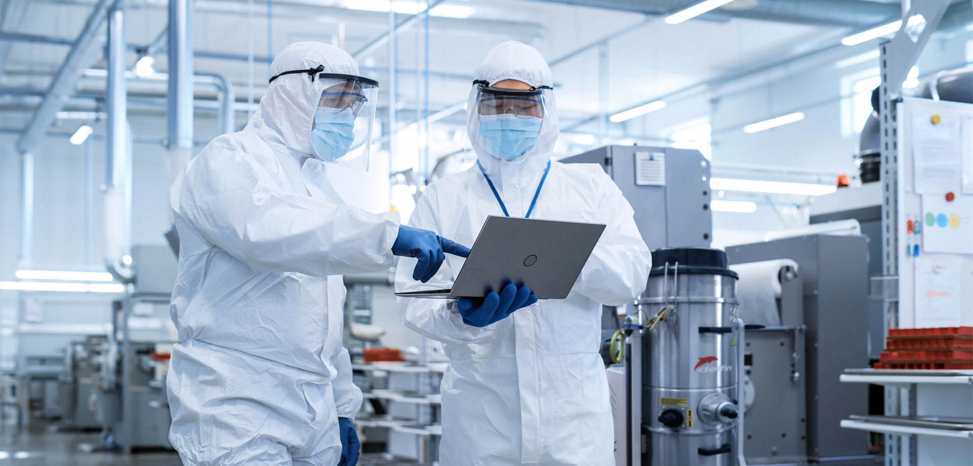 Two professionals in white PPE discussing a vacuum cleaner in a production environment