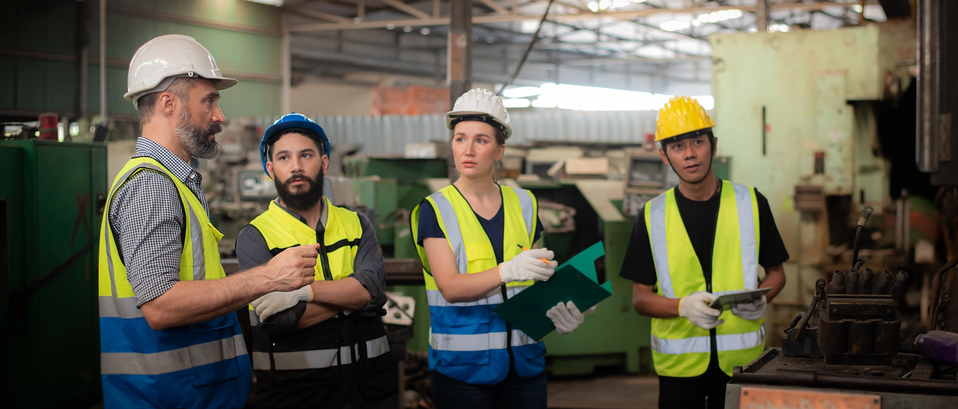 Four industrial workers in safety vests discussing ATEX conditions in a production hall