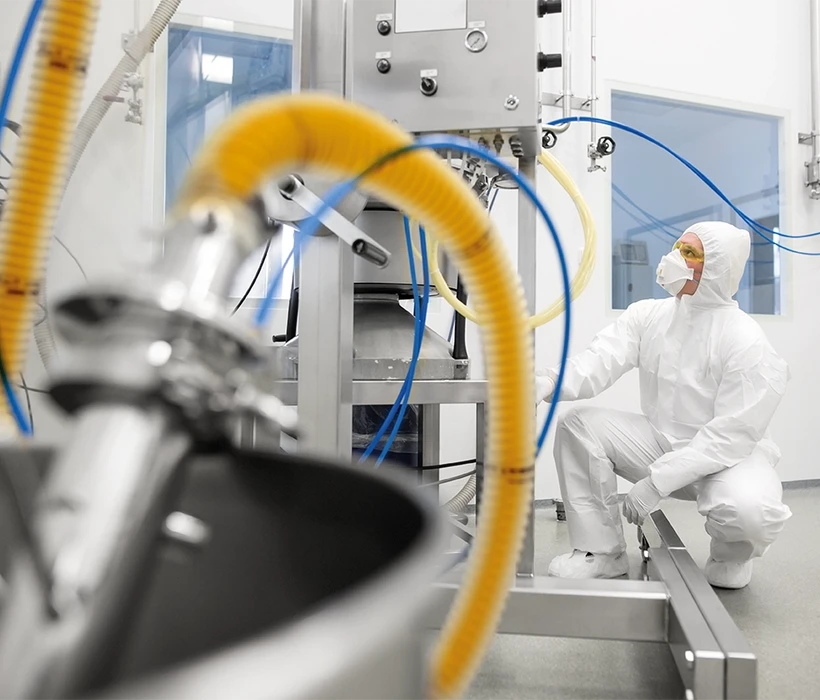 Tekniker i renrumsdragt arbejder med tekniske slanger i farmaceutisk produktionsmiljø