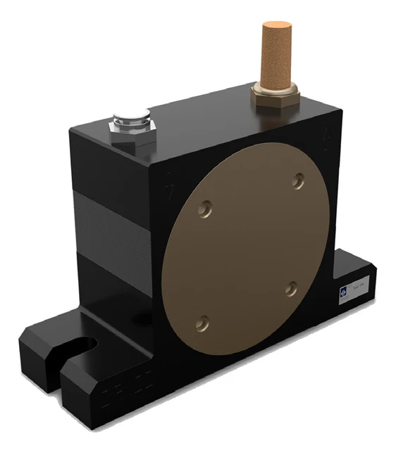 A roller vibrator seen from the front at an angle: a black anodised aluminium body, clearly wider than it is tall, with a large round brass cover in the middle of the side. Four countersunk holes sit near the rim of the cover. On top are two connections: on the left a push-in fitting, on the right a brass nut carrying a sintered bronze silencer. A mark is cast into the front face under each connection: on the left a downward triangle, on the right an upward arrow. A small nameplate sits on the right-hand side of the body. At the bottom the body meets a wide foot with an open slot in the end.