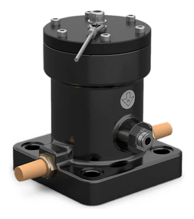 A continuous impact vibrator in the largest version, seen from the front at an angle: a matt black cylinder on an almost square foot with counterbored holes in the corners, a brass silencer on each side, a push-in air connection on the body, and on top a black cover with a ring of bright screws, a hexagonal nut in the middle and a thin rod lying at an angle across the cover.