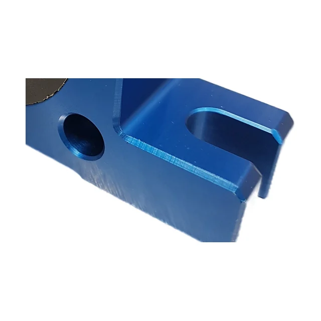 Close-up of one end of the foot on a blue anodised ball vibrator: on the left a round through hole with a chamfered edge, on the right an open slot running right out to the end of the foot. The machining marks are clearly visible in the surface.