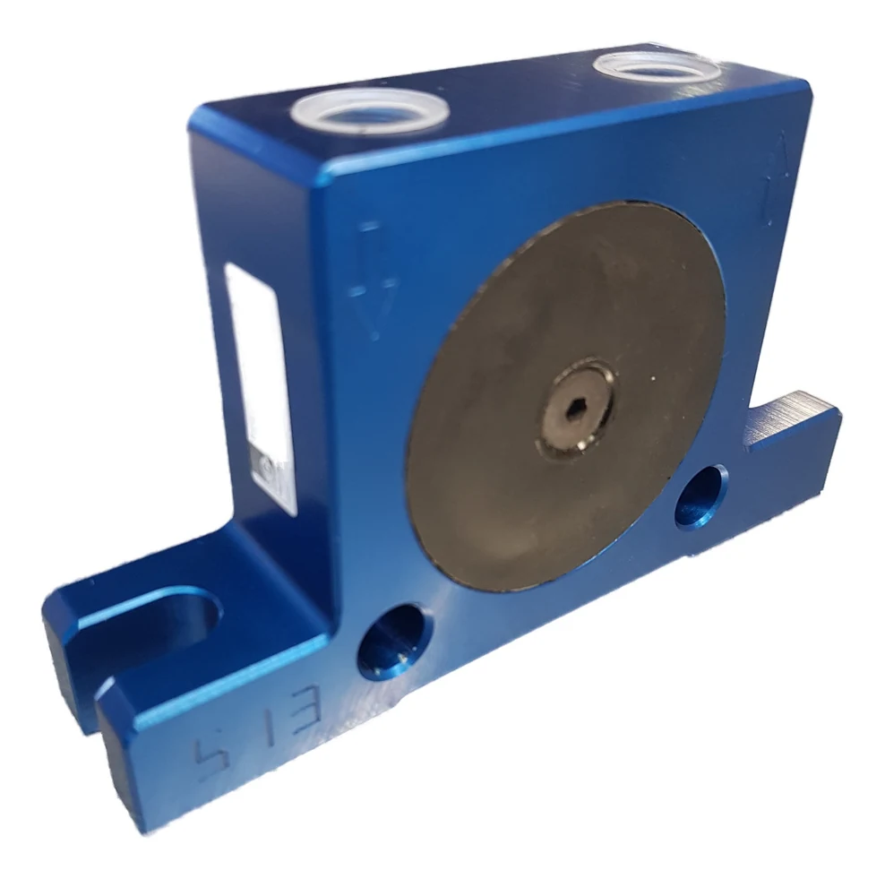 A ball vibrator S 13 seen from the front at an angle: a blue anodised aluminium body, a third wider than it is tall, with a dark round cover and a central screw in the middle of the side. On top sit two threaded ports with bright rings. At the bottom the body meets a wide foot with a round through hole at each end and an open slot outermost at each end. S 13 is cast into the foot.