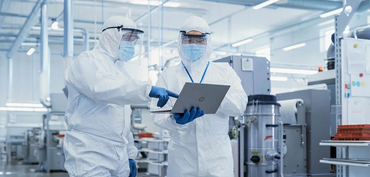 To fagfolk i beskyttelsesdragter konsulterer hinanden i en pharmaproduktion