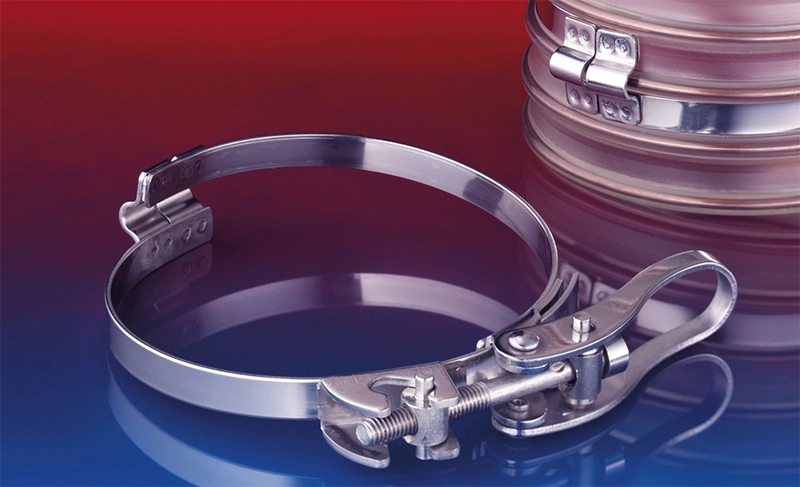 NORRES CLAMP 213 brospændebånd med hurtiglås – vist åbent på bord, viser bro-geometri og lukket montering på slange.